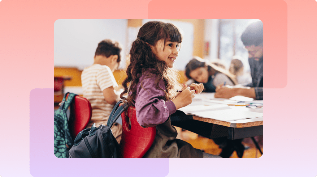 Child smiling at her desk in a classroom.