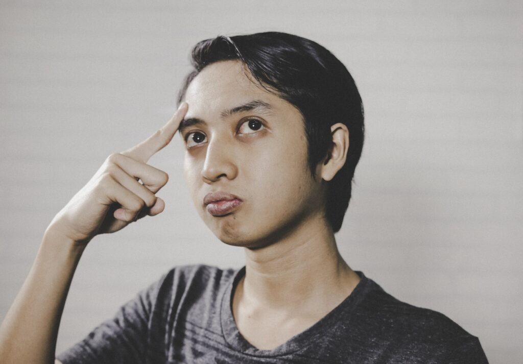 A young woman places index finger on forehead and looks to the upper left quadrant of her vision. She is deep in thought and looks perplexed. 